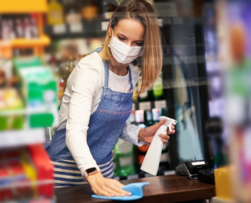 Image of a worker in a grocery store sanitizing a checkout counter.