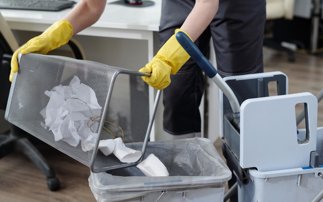 Image of a cleaning service person emptying office trash bins.