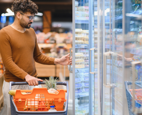 Man Opening Refrigerator In Supermarket While Shopping For Groceries